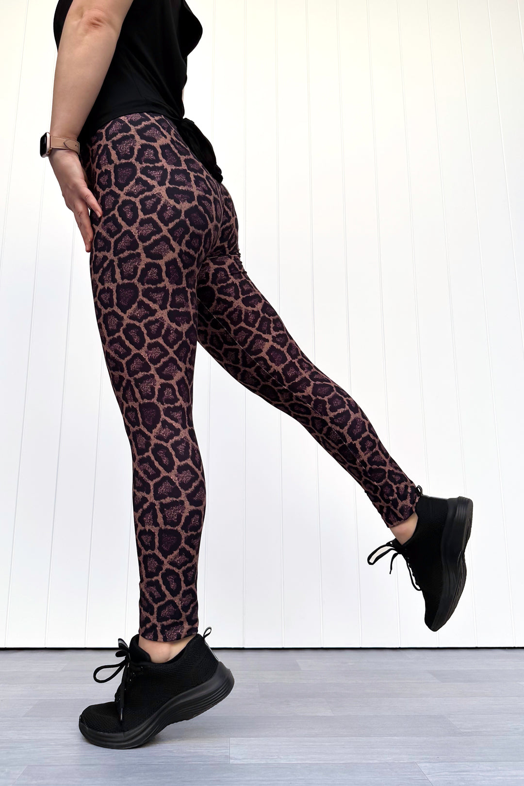 Person wearing leopard print leggings and black shoes against a white wall.