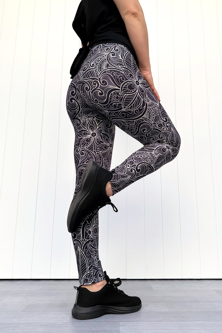 Person wearing black and white patterned leggings with black shoes on a light wooden floor.
