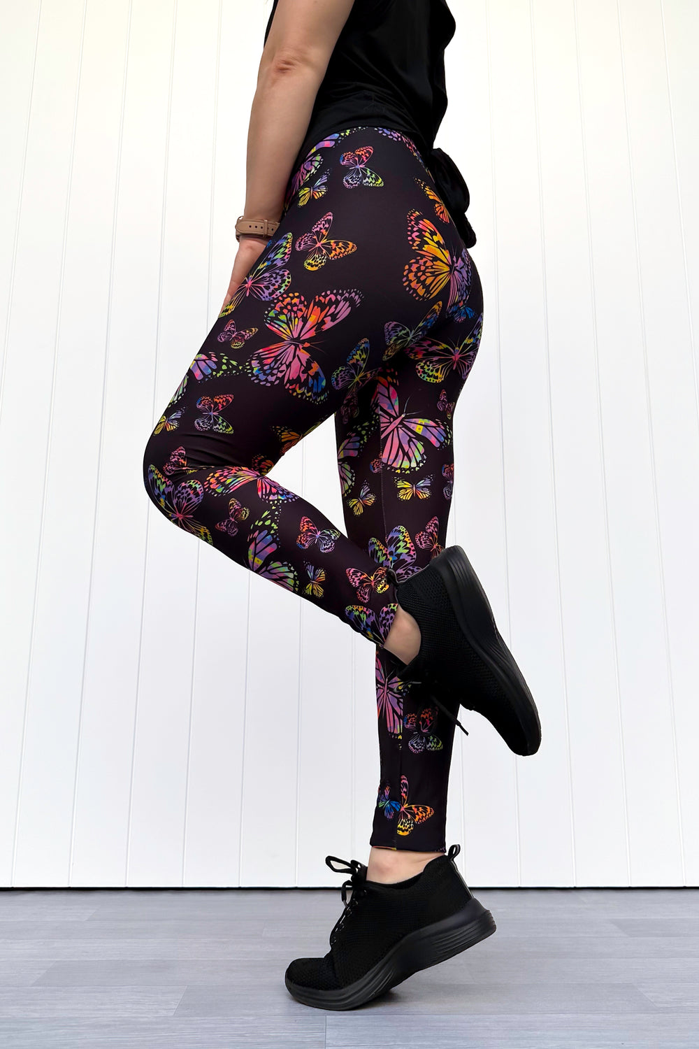 Person wearing black leggings with colorful butterfly pattern against a white background