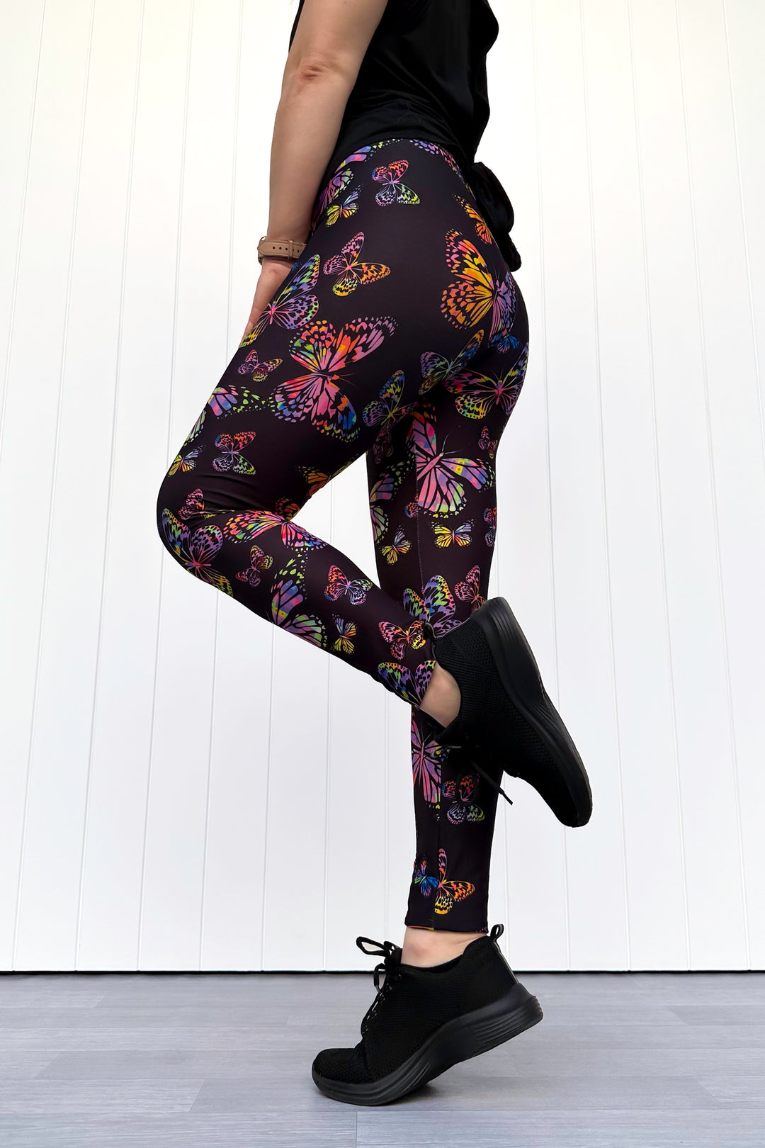 Person wearing black leggings with colorful butterfly pattern against a white background