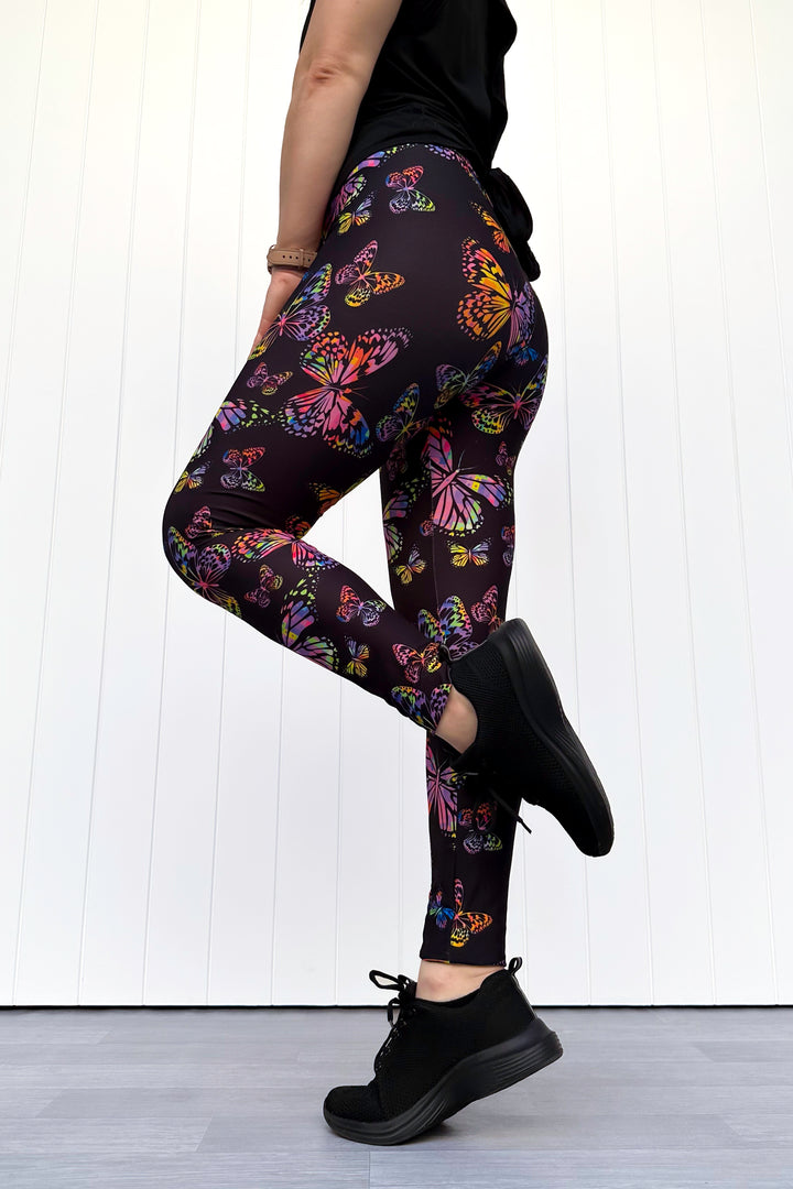 Person wearing black leggings with colorful butterfly pattern against a white background
