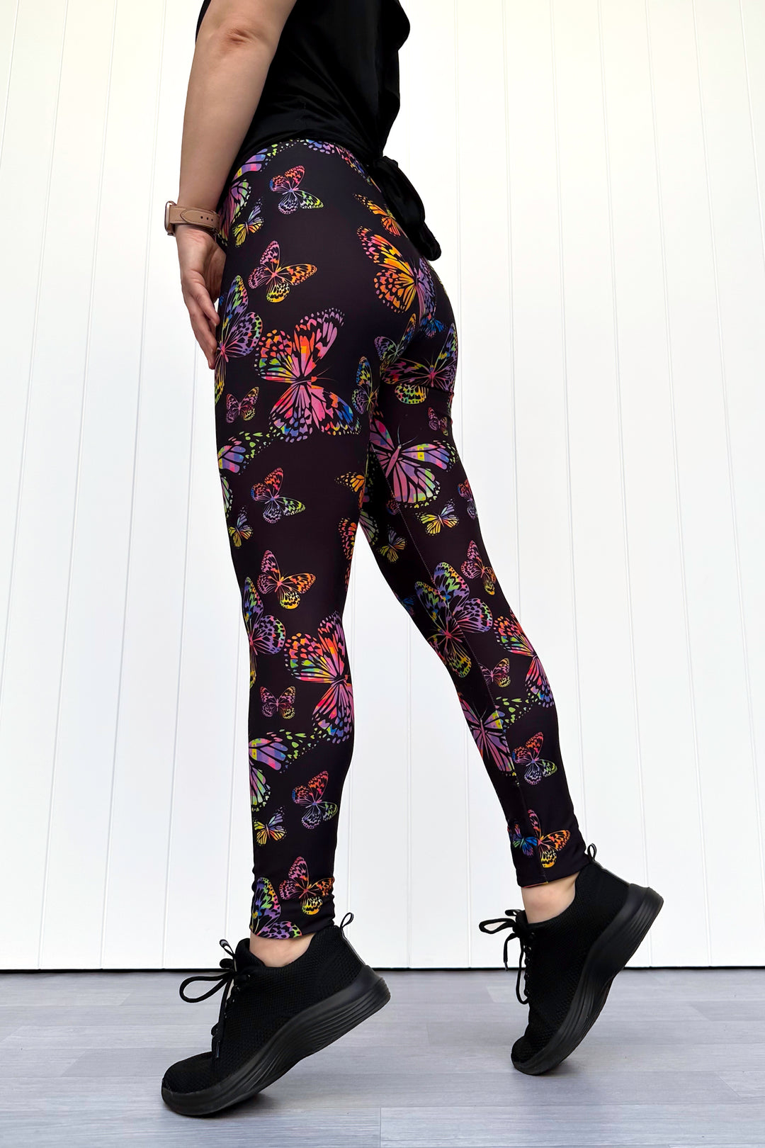 Person wearing black leggings with colorful butterfly pattern against a white background