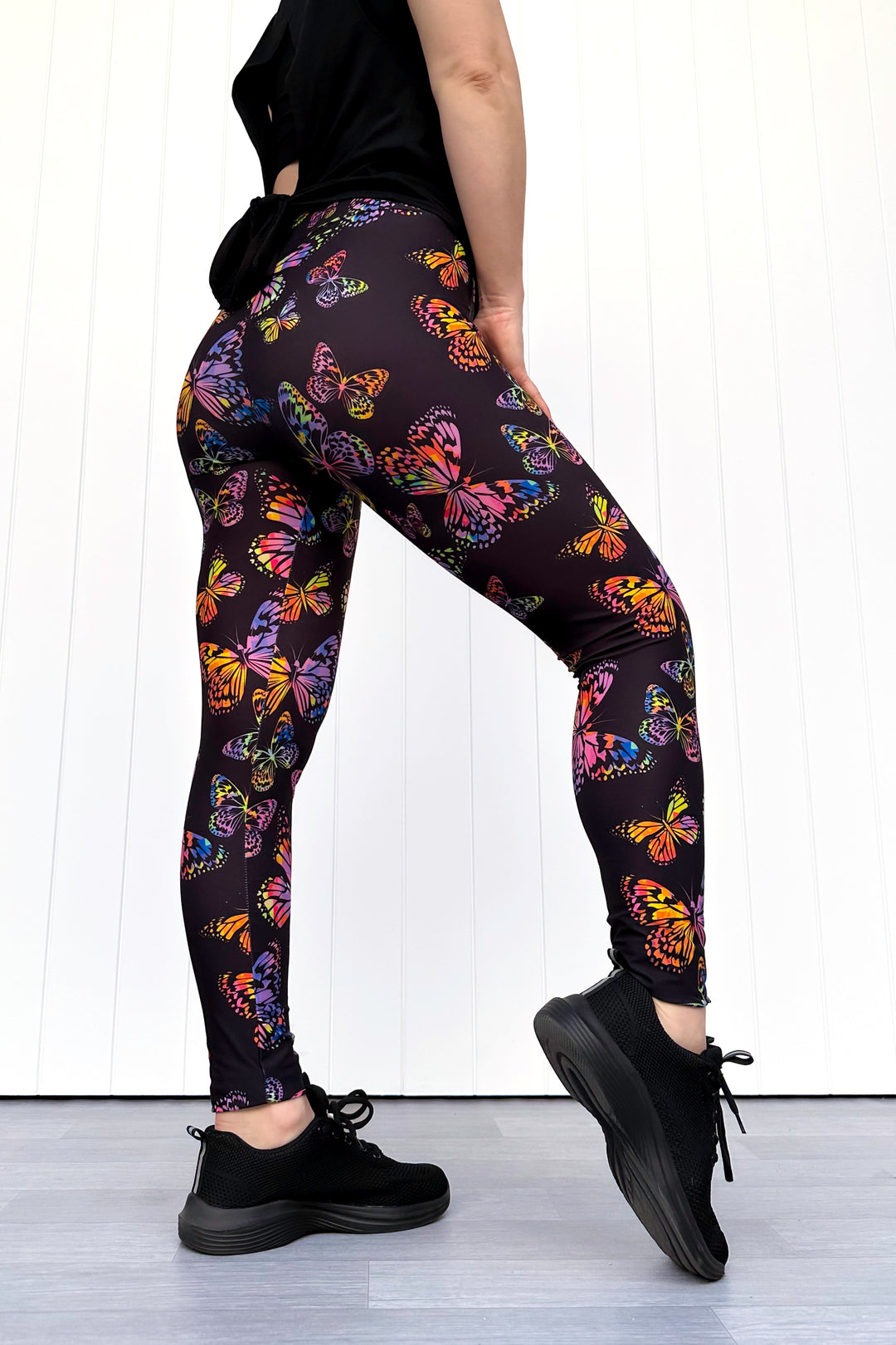 Person wearing black leggings with colorful butterfly pattern on a white background