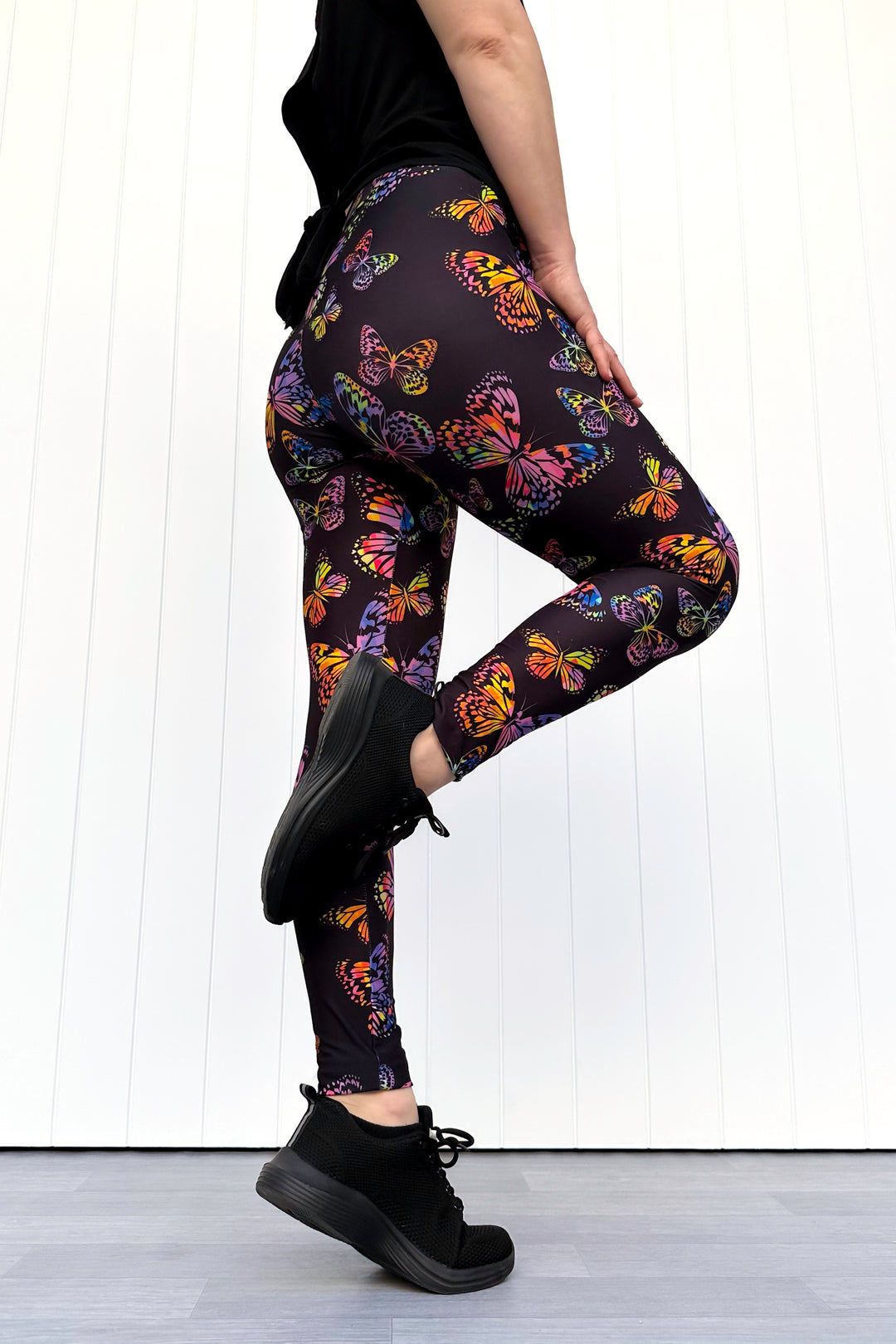 Person wearing black leggings with colorful butterfly pattern on a white background