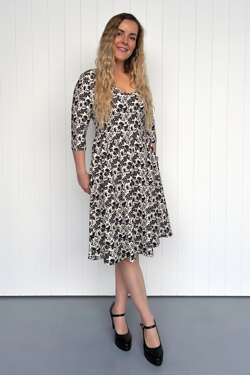 Woman wearing a floral dress against a white paneled wall.